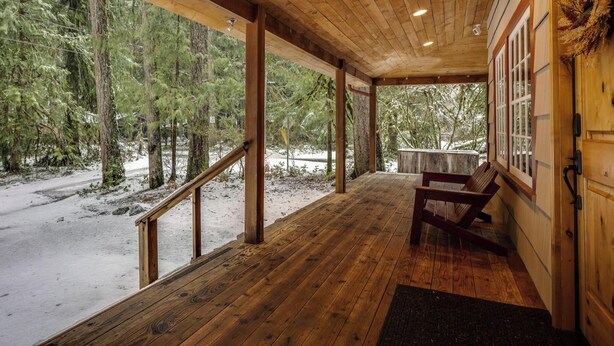 Una terraza de madera con un banco, rodeada de árboles y un paisaje nevado.
