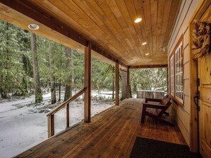 Eine Holzterrasse mit einer Bank, umgeben von Bäumen und verschneiter Landschaft.