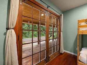 Ein Zimmer mit einem großen Fenster mit Holzrahmen, einem Etagenbett und Blick auf eine bewaldete Landschaft.