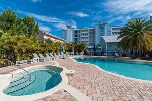 A pool area with lounge chairs and a hot tub, surrounded by palm trees and a building with multiple balconies. - Portside Elite Studio (Merritt Island)