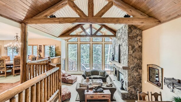 A spacious living area with a high wooden ceiling, stone wall, large windows, and a fireplace. - 5 BDR Forest Retreat w/ Hot Tub (Breckenridge)