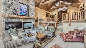 A stone fireplace, a wooden staircase, and a living room with sofas and a coffee table. - 5 BDR Forest Retreat w/ Hot Tub (Breckenridge)