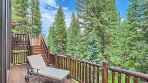 A wooden deck with a lounge chair, a wooden staircase, and a view of tall evergreen trees. - 5 BDR Forest Retreat w/ Hot Tub (Breckenridge)
