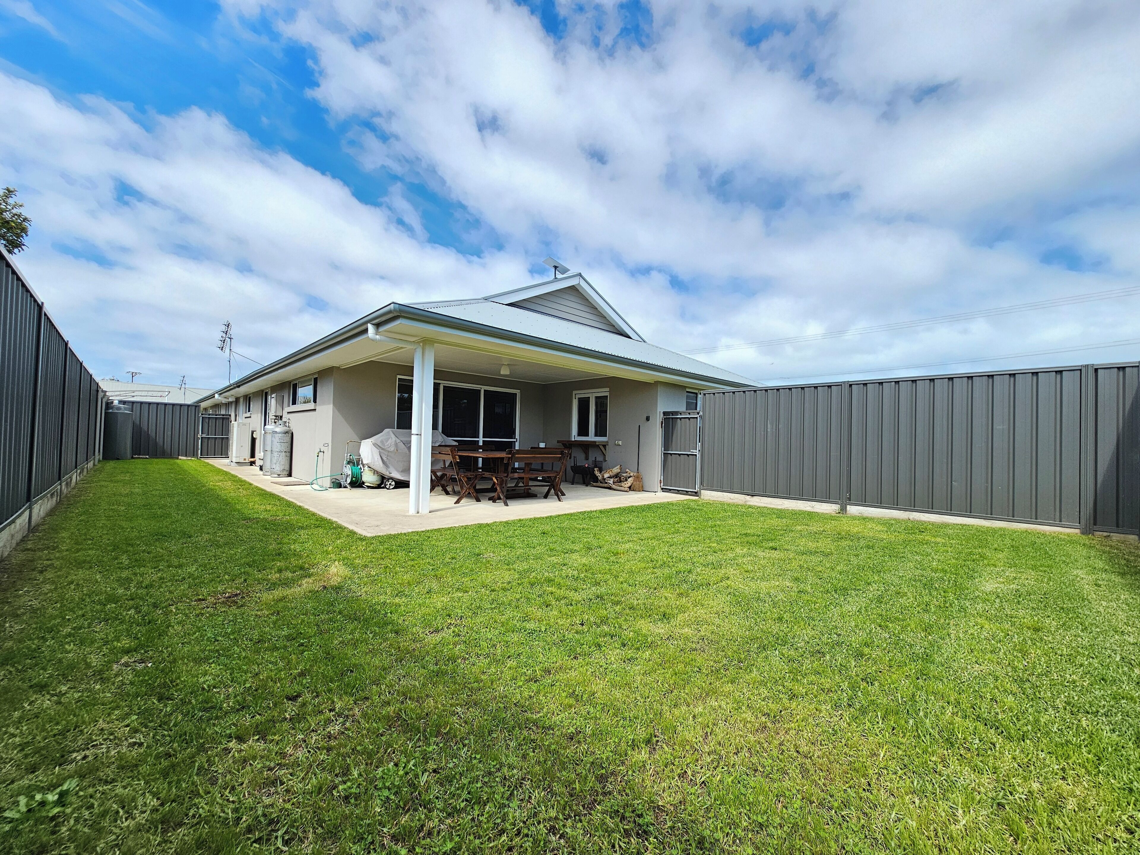 A residential backyard with a covered patio, a lawn, and a grey fence.