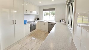 A modern kitchen with white cabinets, a built-in oven, a dishwasher, and a large window providing natural light. - Julia's - Close to the heart of Robe (Robe)