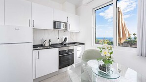 Una cocina moderna con armarios blancos, una encimera negra y vistas al mar a través de una ventana.