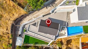Vista aérea de un edificio moderno con piscina en la azotea, cancha de tenis verde y un marcador rojo de ubicación.