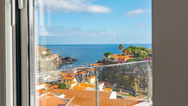 Vista costera desde un balcón con edificios, cielo despejado y el mar.