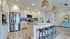 A modern kitchen with stainless steel appliances, a central island with bar stools, and pendant lighting.