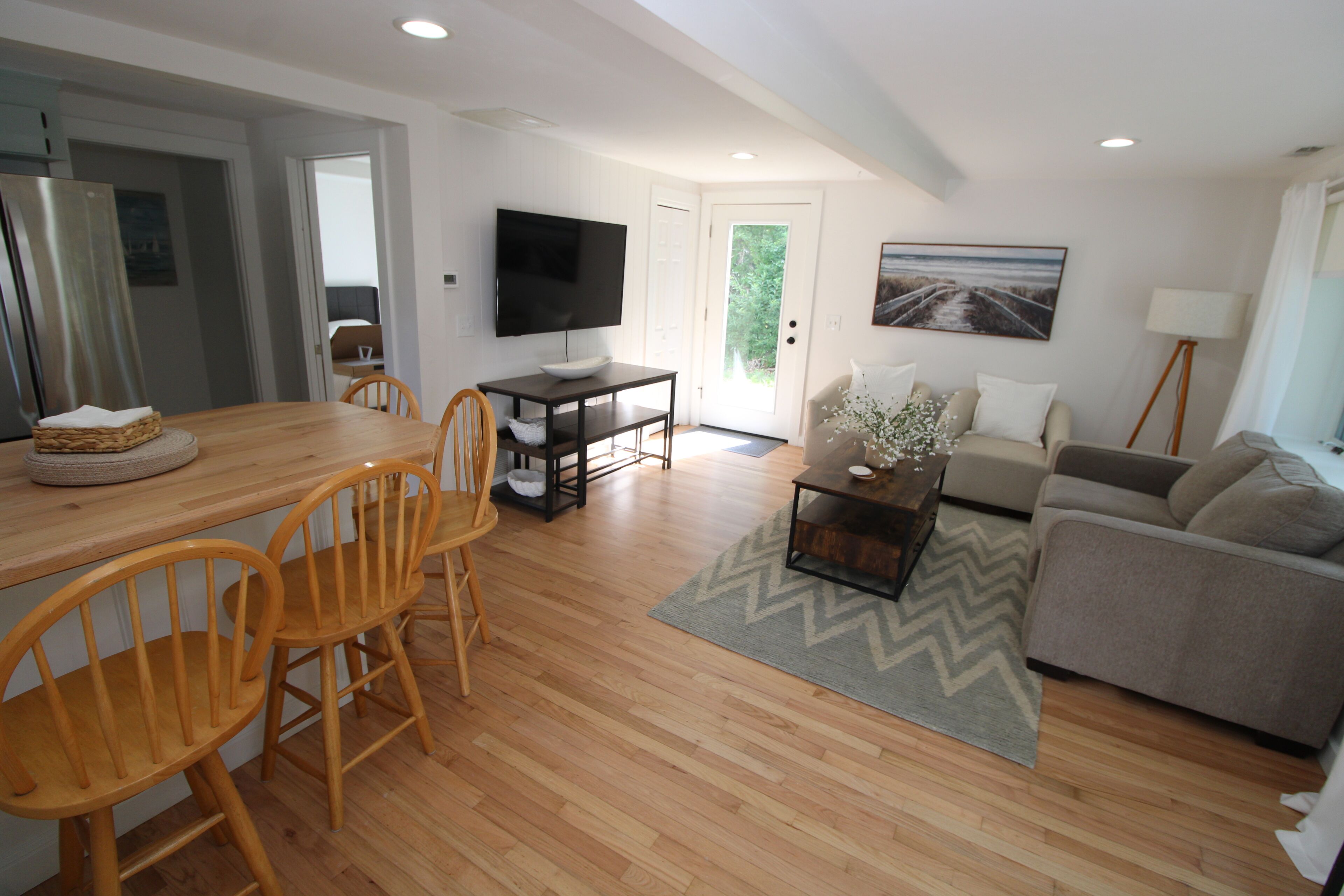A modern living room with a wooden dining table, chairs, a sofa, a coffee table, and a TV.