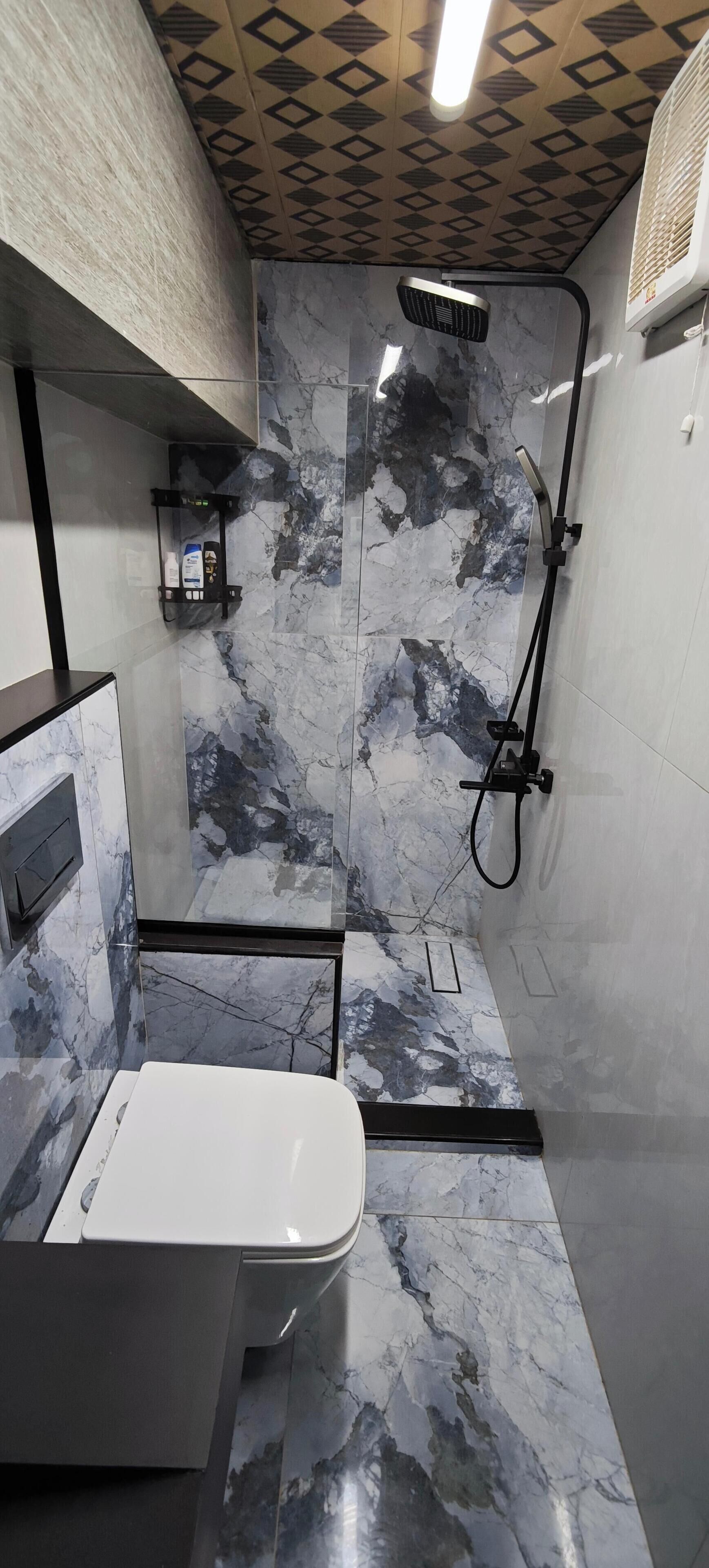 A modern bathroom with a shower, marble walls, and a toilet.