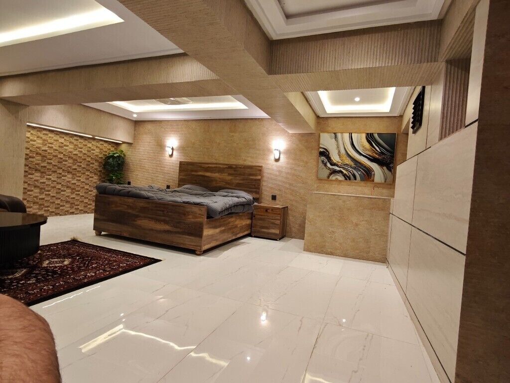 A modern bedroom with a wooden bed, a nightstand, a wall-mounted TV, and a large window.