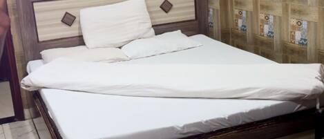 A neatly made bed with a wooden headboard, a bedside table, and a wall-mounted fan.