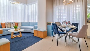 Un salon moderne avec un canapé bleu, une table basse ronde et un coin repas comprenant une table et des chaises en verre.