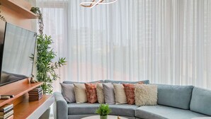 Un salon moderne avec un canapé gris, un téléviseur à écran plat posé sur un meuble en bois et une table basse ronde agrémentée d’une plante.