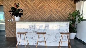 Un espace d’accueil doté d’un comptoir en marbre, de trois tabourets en bois et d’un mur orné d’un motif en chevrons.