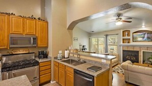 A kitchen with wooden cabinets, a microwave, stove, and dishwasher. There's a dining area with a couch and a fireplace. - Mountain Retreat! ~King Bed w/ Memory Foam ~Fireplace ~Game Table (Flagstaff)