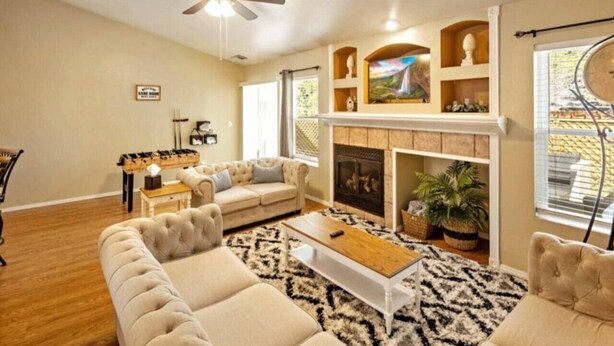A spacious living room with a fireplace, a ceiling fan, and a large window. - Mountain Retreat! ~King Bed w/ Memory Foam ~Fireplace ~Game Table (Flagstaff)