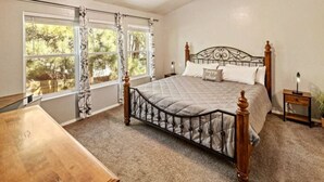 A bedroom with a large bed, a wooden nightstand, a bedside table, and a window with curtains. - Mountain Retreat! ~King Bed w/ Memory Foam ~Fireplace ~Game Table (Flagstaff)