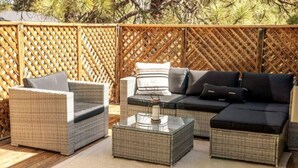 An outdoor seating area with wicker furniture, including a sofa and chairs, and a glass coffee table. - Mountain Retreat! ~King Bed w/ Memory Foam ~Fireplace ~Game Table (Flagstaff)