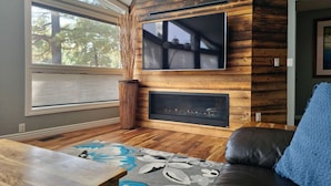 Una sala de estar moderna con una pared de madera, una chimenea, un televisor de pantalla plana y un sofá con un cojín azul.