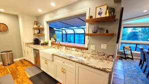 Una cocina moderna con armarios blancos, encimeras de granito y un ventanal con vistas a una terraza.