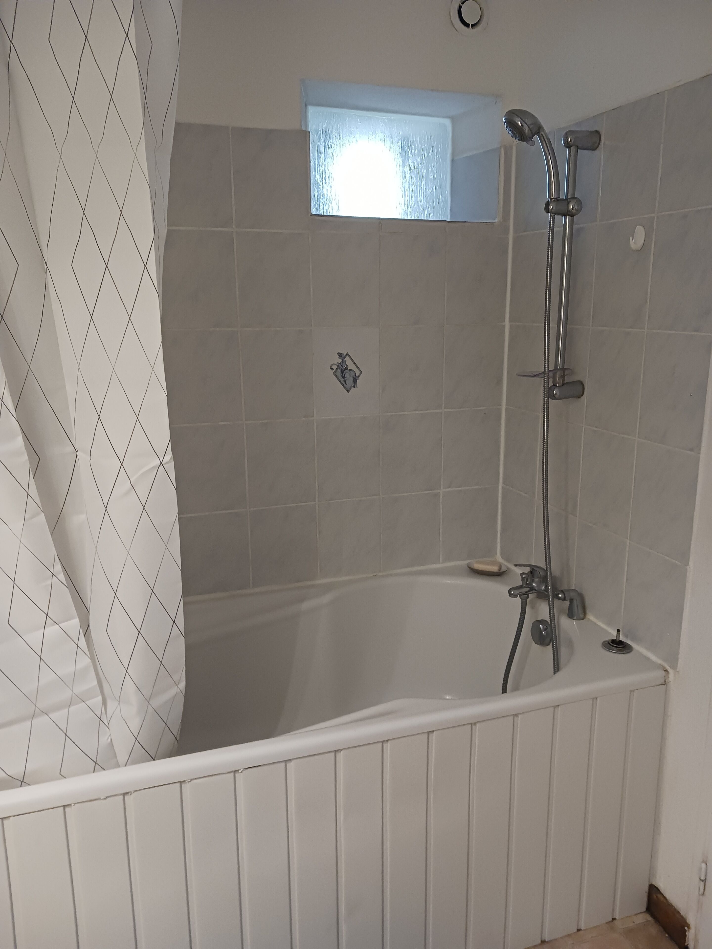 A bathroom with a bathtub, shower, and a small window.