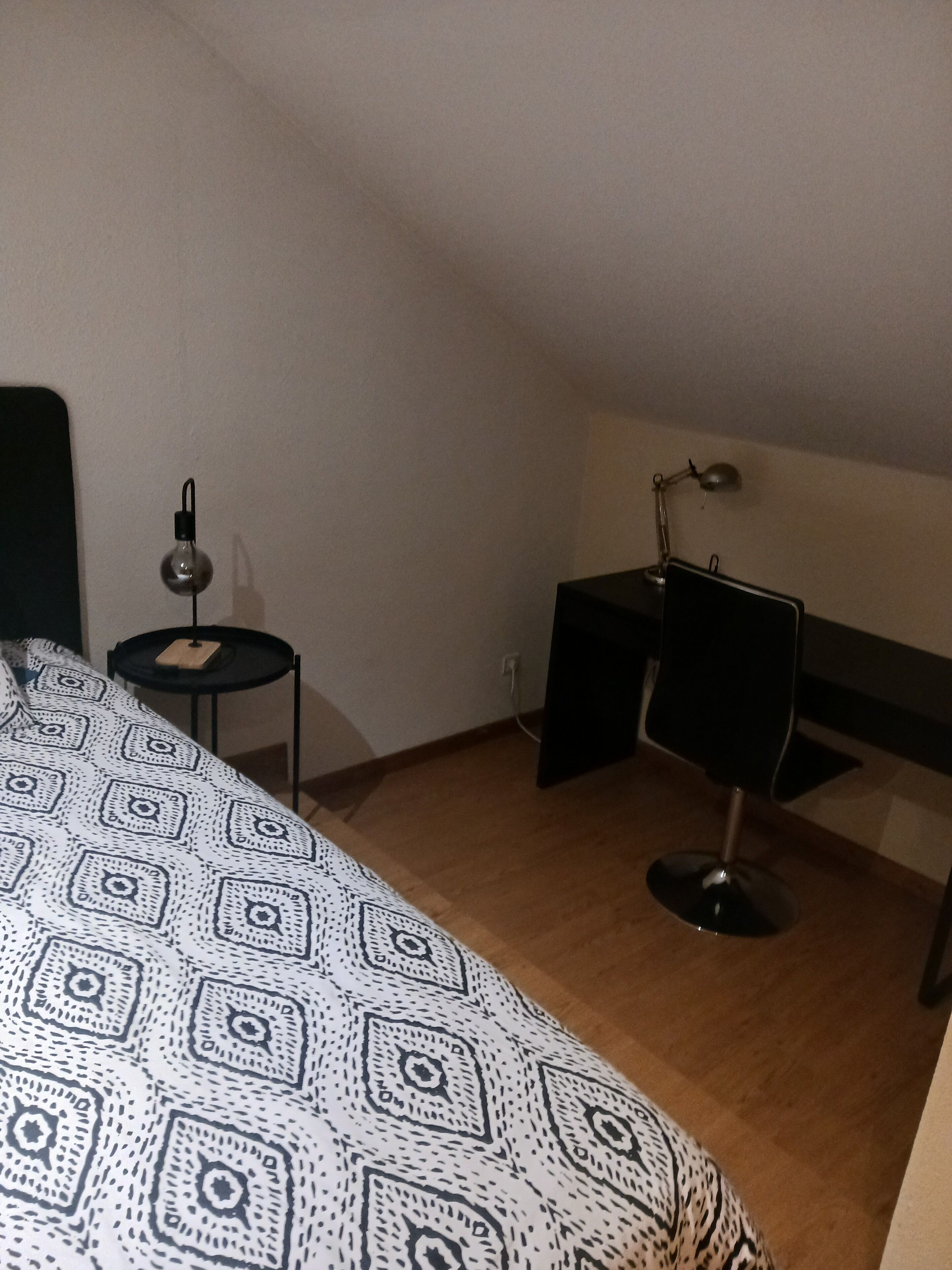 Une chambre avec une couvre-lit à motifs, un bureau avec une lampe et une petite table également dotée d’une lampe.