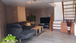A modern living room with a grey sofa, a wooden coffee table, a TV on a black stand, and a staircase with a wooden railing.