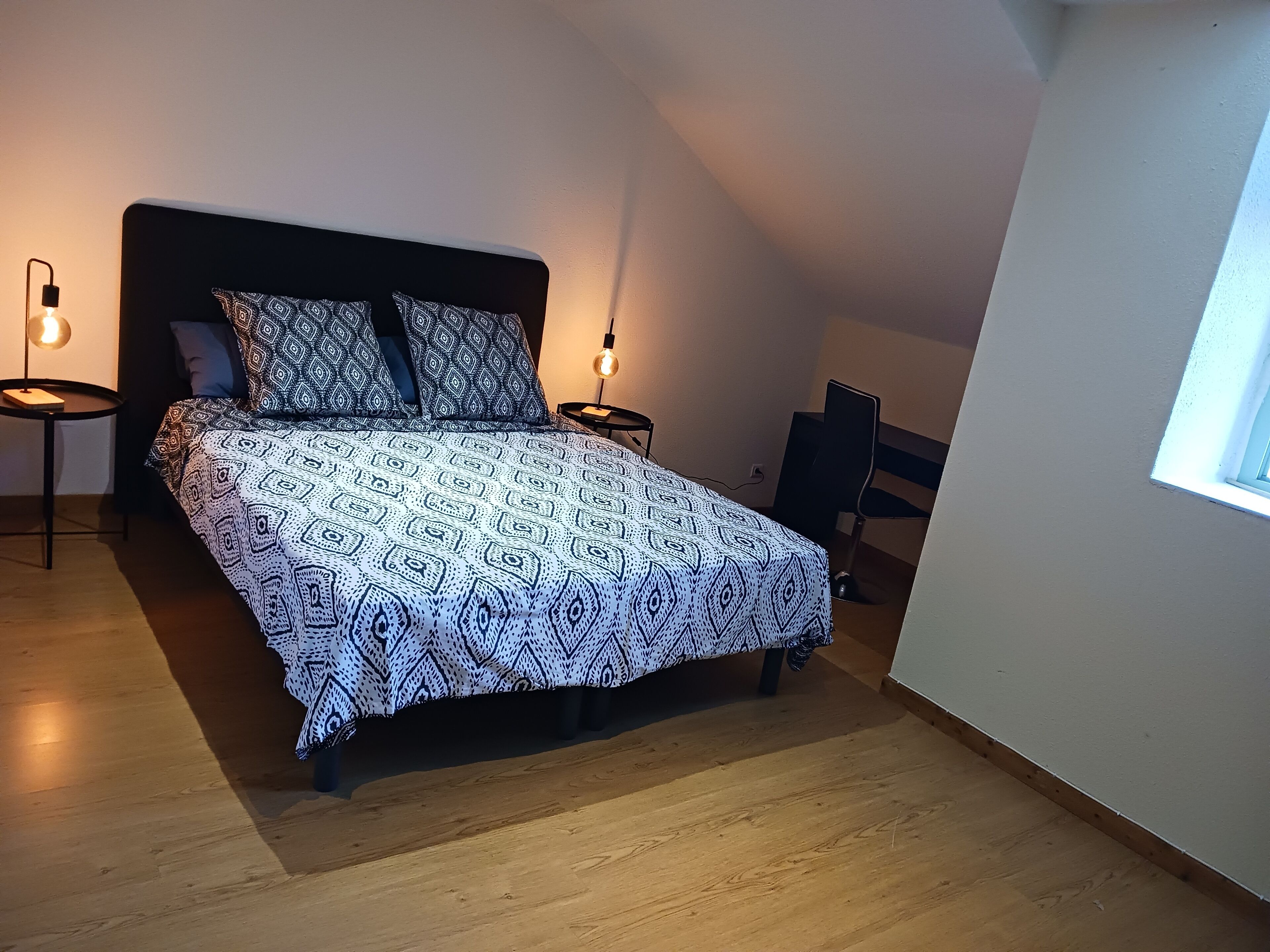 Une chambre à coucher avec un lit, deux tables de chevet, une chaise et une fenêtre.
