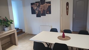 A dining area with a white table and black chairs, a world map on the wall, a potted plant, and a radiator.