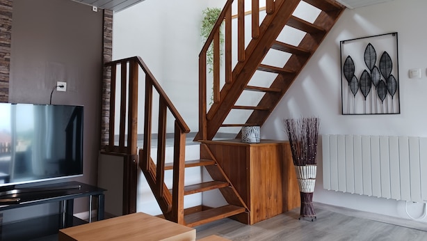 A modern living room with a wooden staircase, a flat-screen TV, a wooden table, and a radiator.