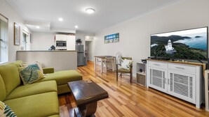A modern living room with a green sofa, a wooden coffee table, and a television on a cabinet.