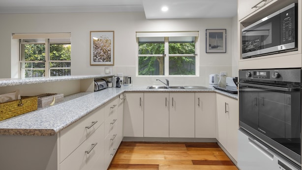 A modern kitchen with white cabinets, granite countertops, a stainless steel oven, and a window with a view of greenery.