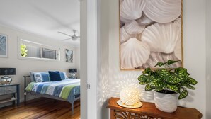 A bedroom with a bed, bedside tables, a ceiling fan, a window, and a wall-mounted artwork.