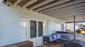 A covered patio with a white fence, a gray sofa with blue pillows, and a wooden bench.