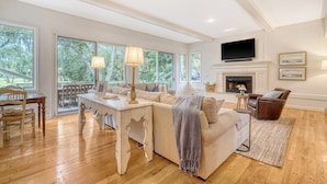A spacious living room with a fireplace, large windows, and a television. - New rental, great Vanderhorst home (Kiawah Island)