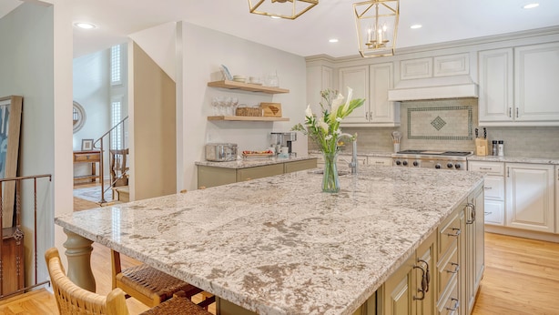 A spacious kitchen with white cabinetry, a large granite island, and modern pendant lighting. - New rental, great Vanderhorst home (Kiawah Island)