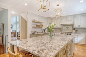 A spacious kitchen with white cabinetry, a large granite island, and modern pendant lighting. - New rental, great Vanderhorst home (Kiawah Island)