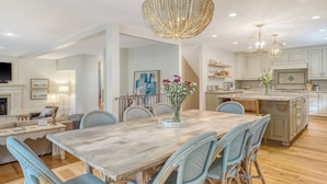 A spacious dining area with a wooden table and wicker chairs, a chandelier, and a kitchen with white cabinets and a central island. - New rental, great Vanderhorst home (Kiawah Island)