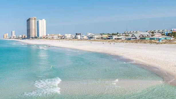 Ein Strand mit klarem türkisblauem Wasser und einem Sandstrand. Im Hintergrund sind hohe Gebäude zu sehen.