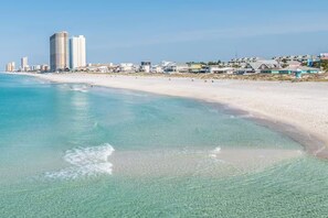 Uma praia com águas turquesa cristalinas e areal dourado. Edifícios altos estão visíveis ao fundo.
