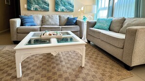 Ein Wohnzimmer mit zwei Sofas, einem Glastisch und einem Teppich. An der Wand hängen zwei abstrakte Gemälde.