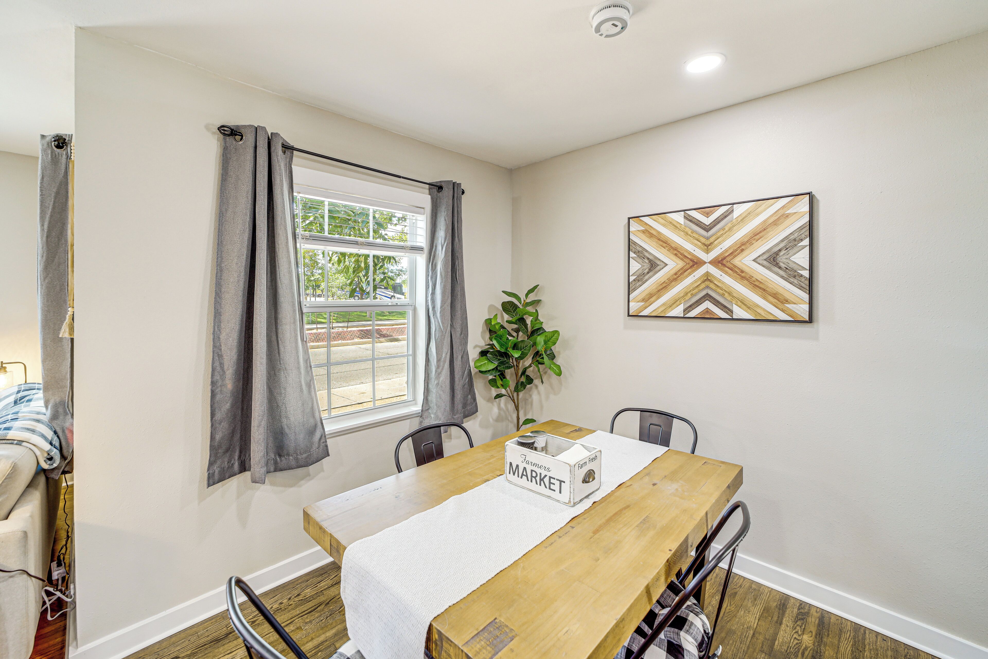 A dining area with a wooden table, chairs, a white tablecloth, a plant, and a geometric wall art piece.
