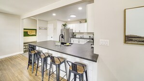 A modern kitchen with a central island, bar stools, and white cabinetry. - Walk to Expo Square Pavilion: Updated Tulsa Home! (Tulsa)