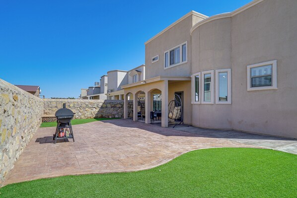 A residential area with a paved driveway, a stone wall, and a barbecue grill.