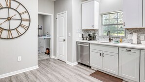 A modern kitchen with white cabinetry, a large wall clock, and a window providing natural light. - Pond + Trails On-site: Washington Escape! (Washington)