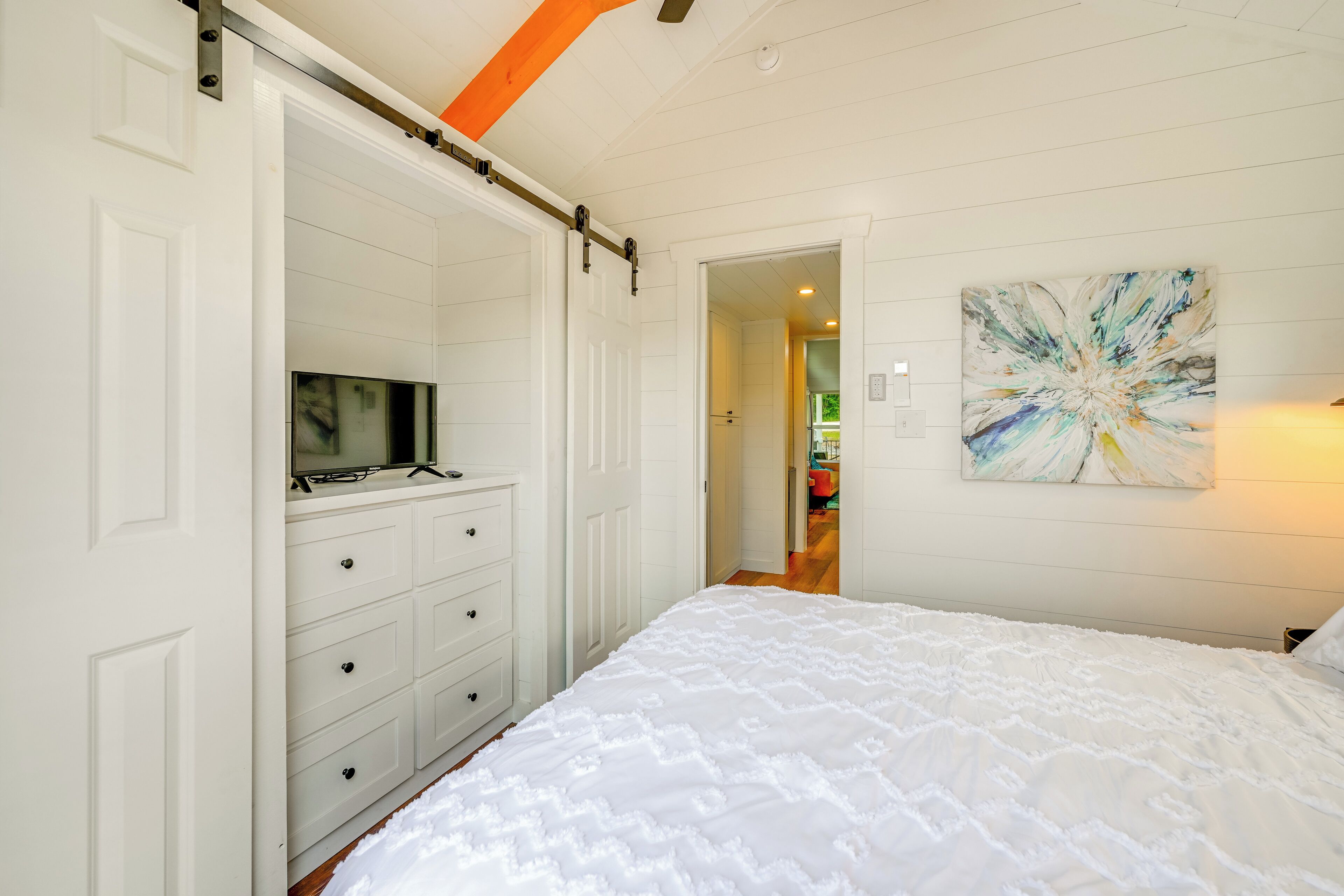 A bedroom with a bed, a dresser, a sliding door, and a painting on the wall.