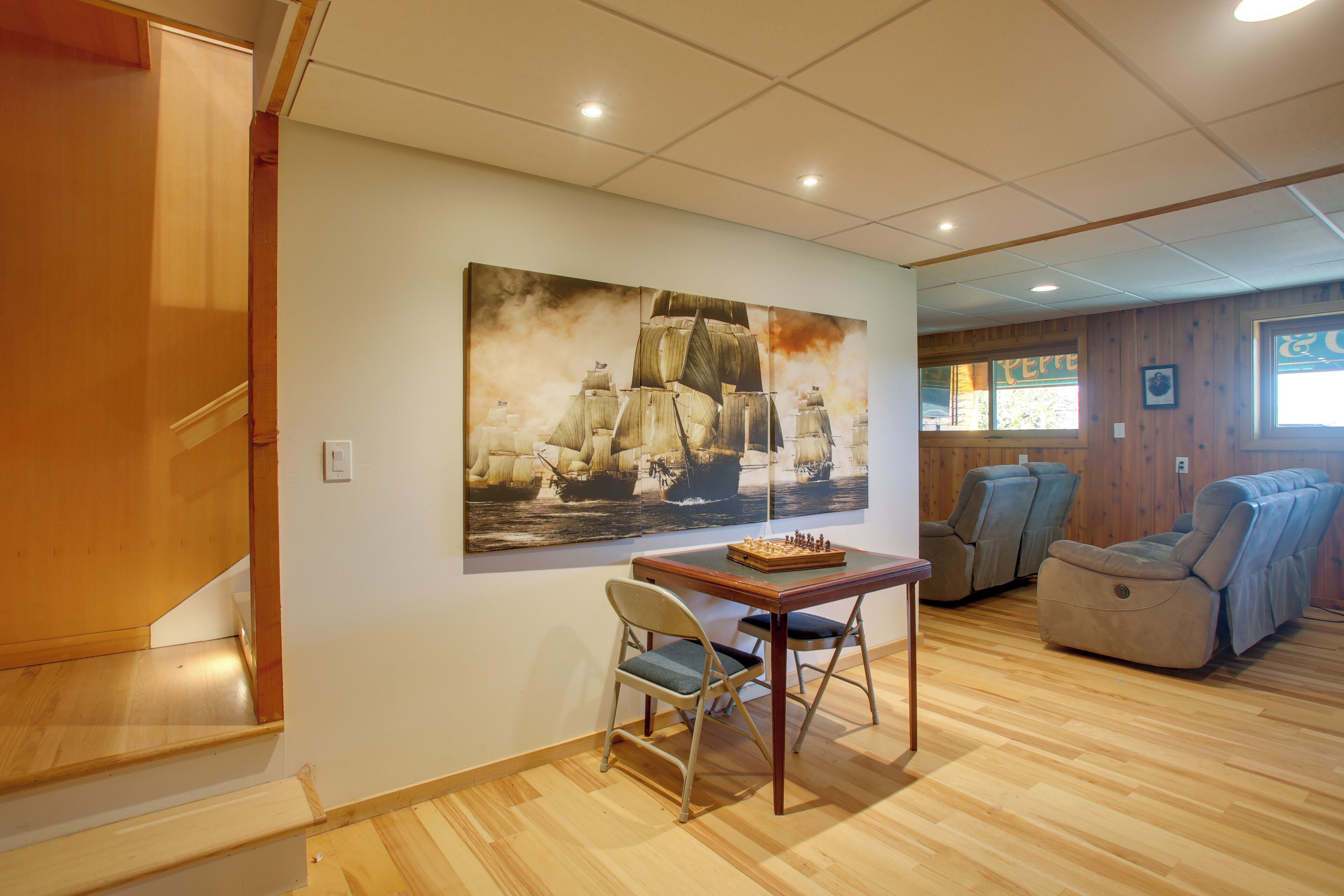 A room with a wooden floor, a table with a chessboard, two chairs, a sofa, and a large painting on the wall.