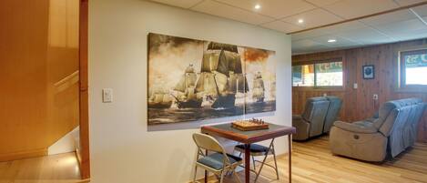 A room with a wooden floor, a table with a chessboard, two chairs, a sofa, and a large painting on the wall.